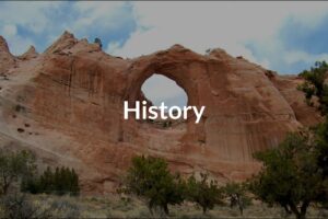 Landscape image of "Window Rock", a large red rock structure with a round hole in the middle with History overlayed on top.